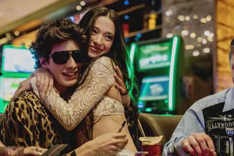 Two characters from Anora hugging while sitting at a casino table